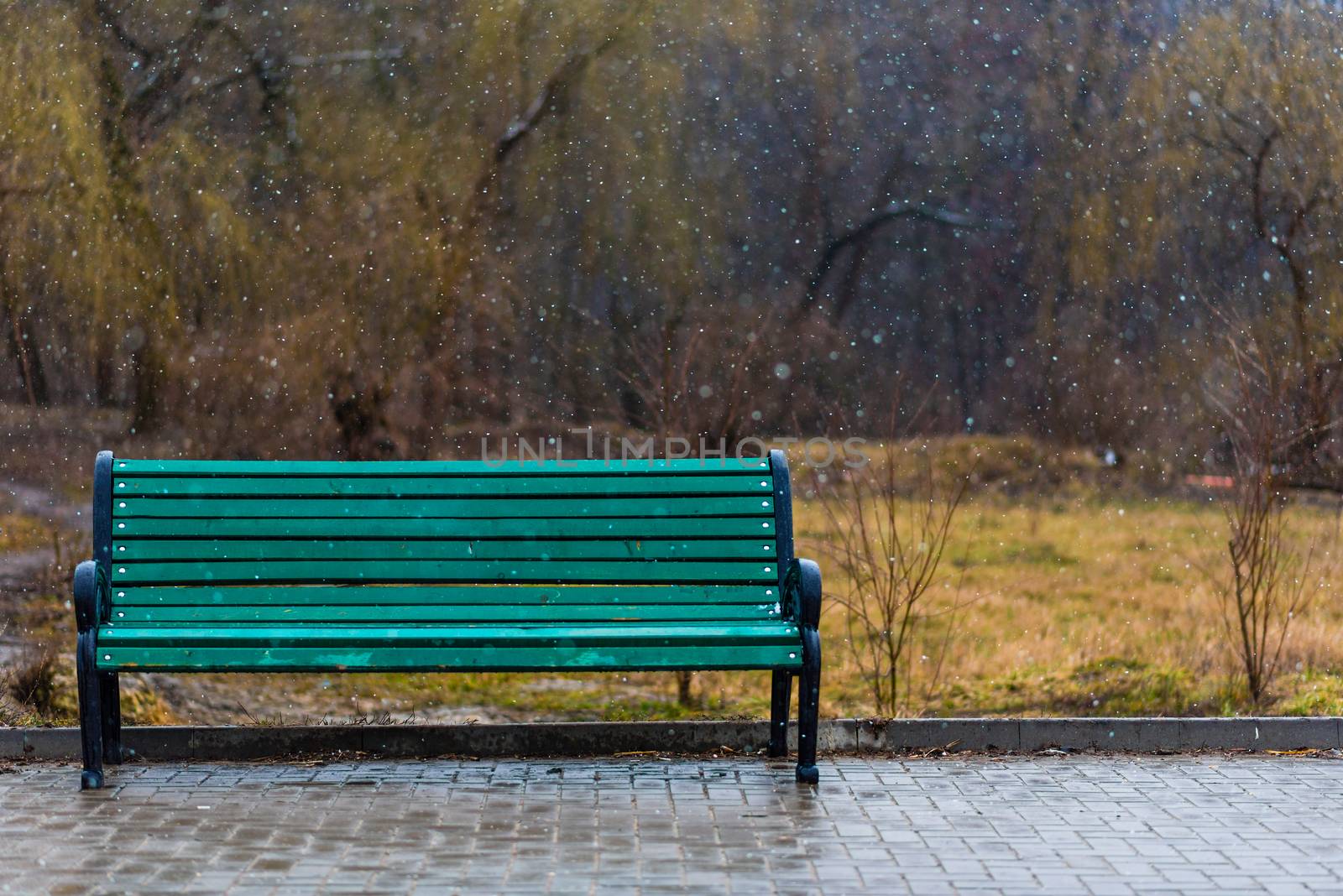 A green bench under falling snowflakes.