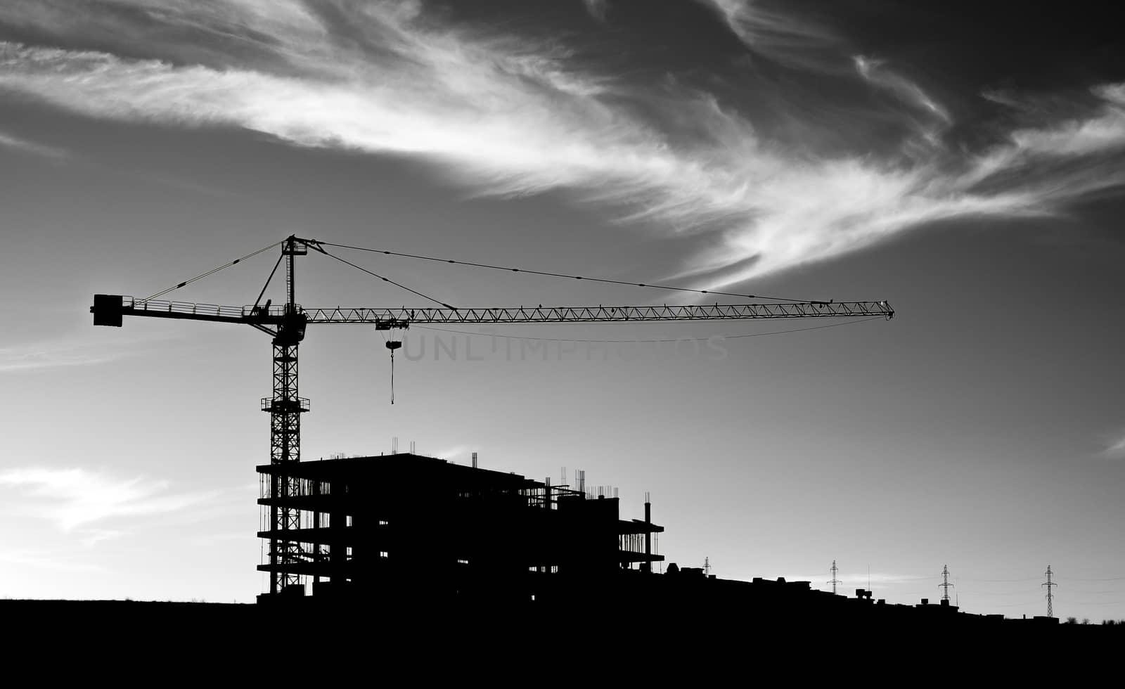 A black and white picture of construction crane under sky with clouds. 