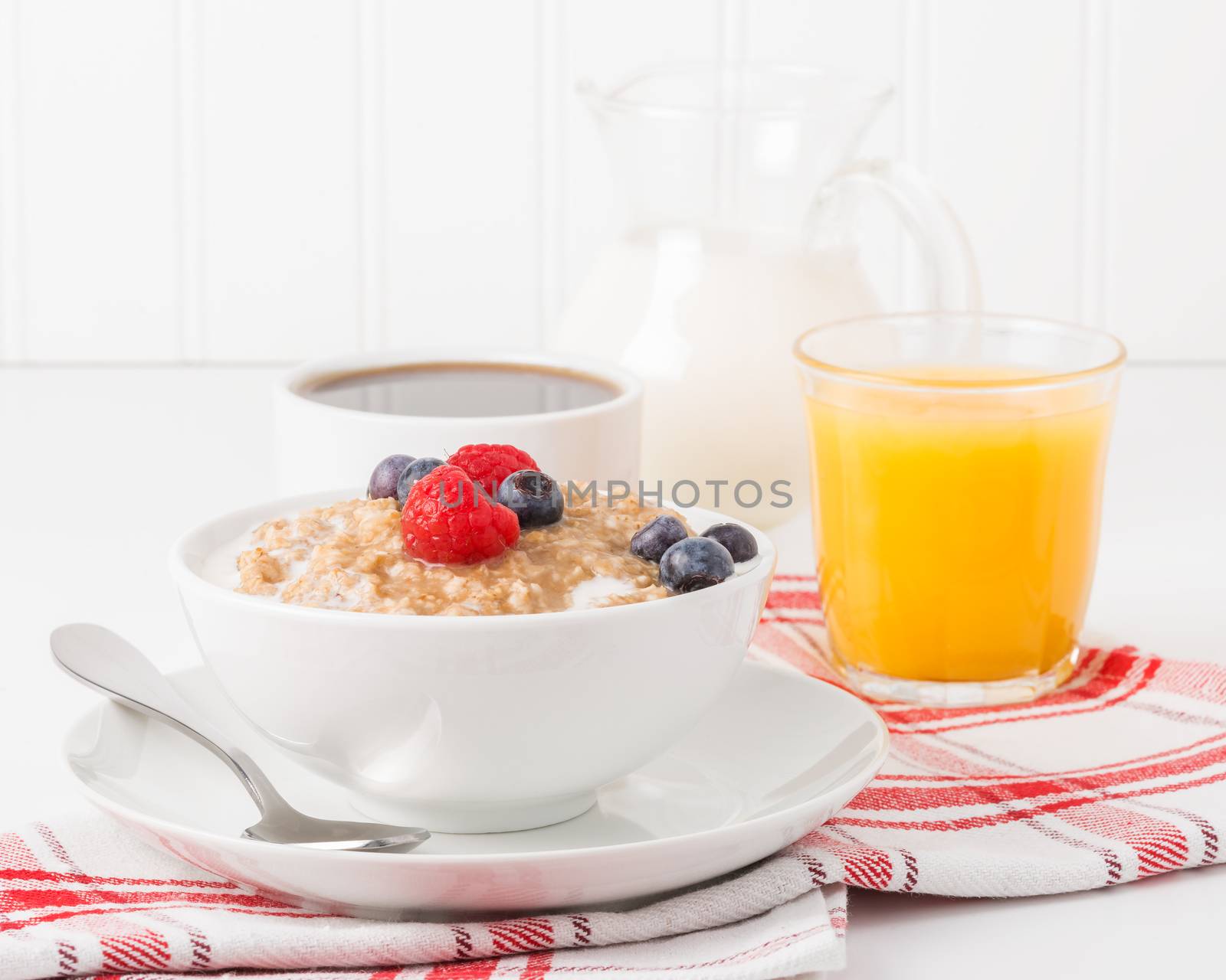 Bowl of oatmeal with fresh berries with coffee and orange juice.