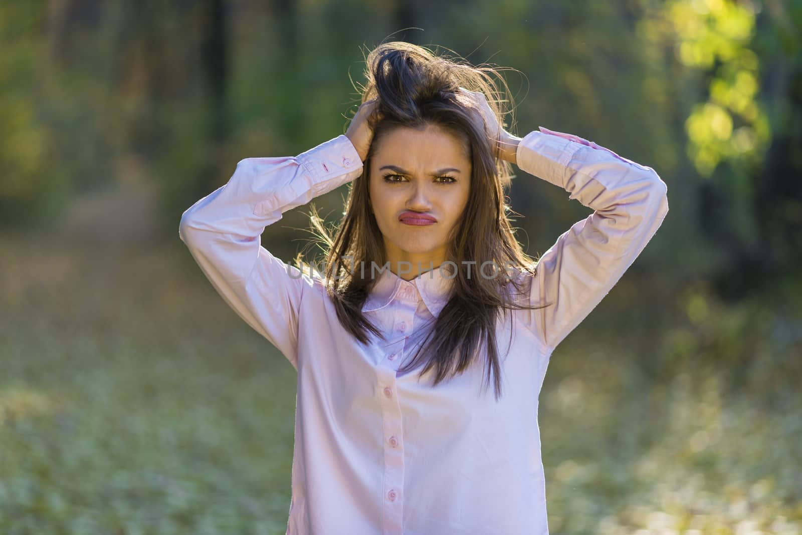 Holding head full of problems. A pretty teenager funny looking girl is holding her head with her hands like her life is full of different problems. Her hair is backlit by the sun.  Action takes place in an autumn forest at afternoon.