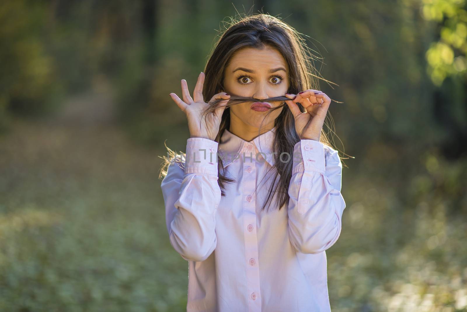 A teenage girl is making mustache from her hair with eyes wide open and a quirky expression on her face.