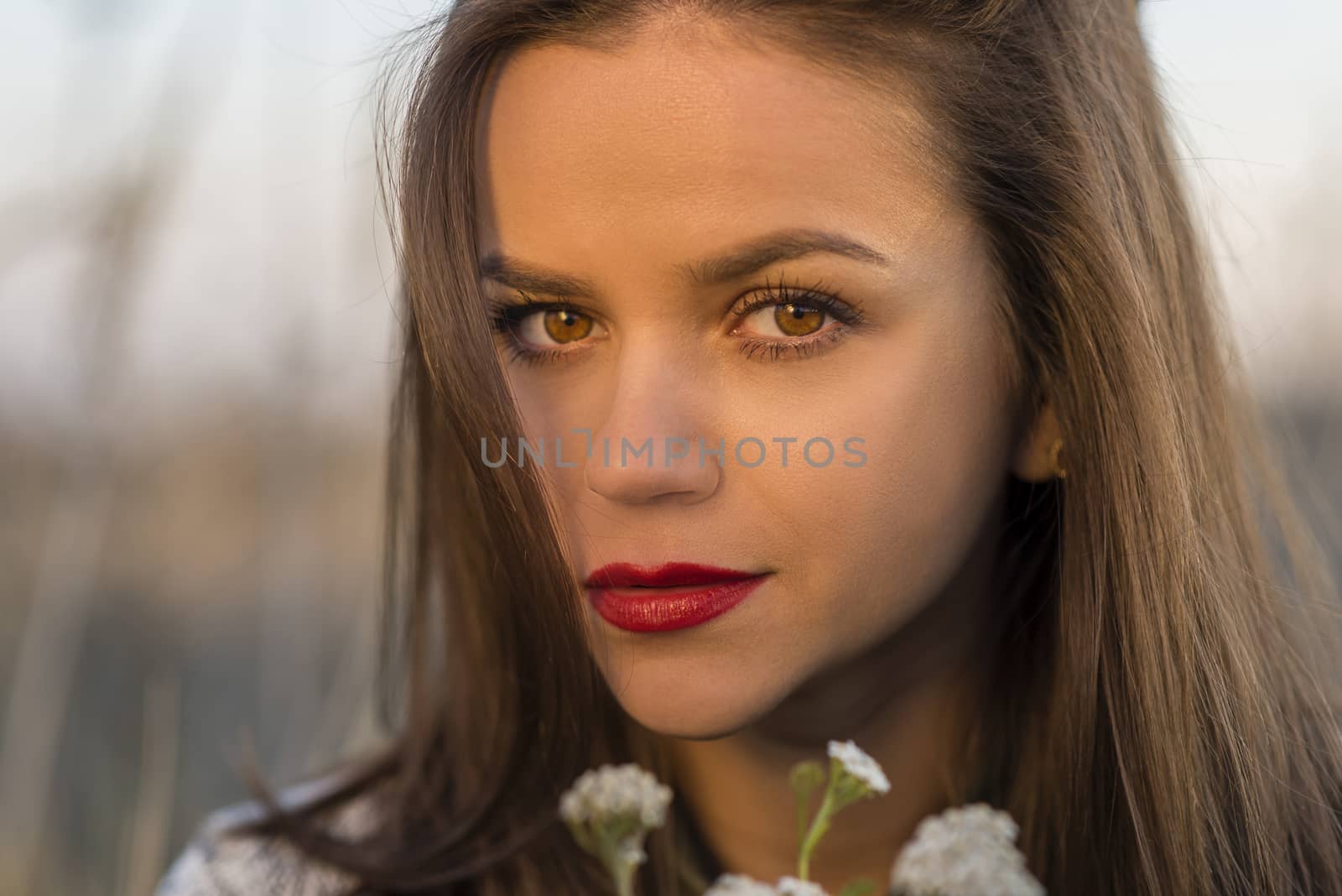 Autumn look. Portrait of a nice teenager girl holding small bouquet in a autumn field. Girl has brown eyes and hair and red lips.