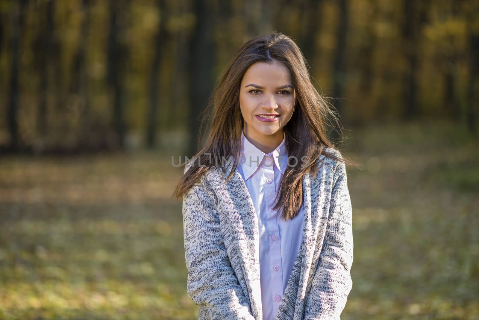 Smiling girl is posing in a autumn forest in a warm knitted blouse. Action takes place in an autumn afternoon.