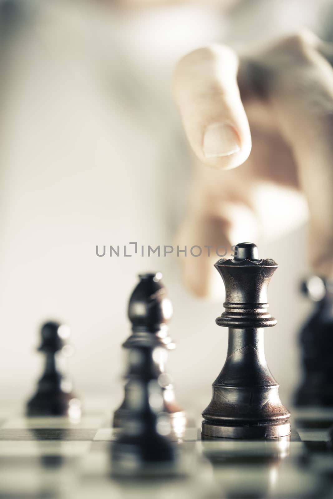 Vertical Image of a chess game with focus on the queen and a blurry hand at the background, Copy space on the left side. Concept of strategic business or risk management.
