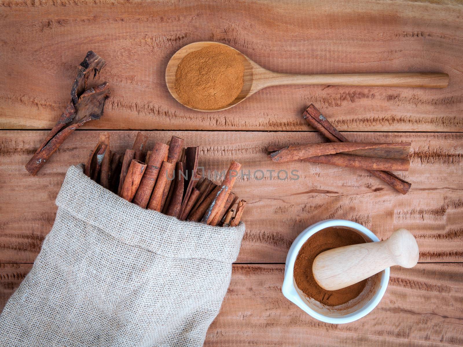 Composition of cinnamon stick in hemp sack and cinnamon powder in white mortar and  cinnamon powder in wooden spoon on rustic old wooden background .