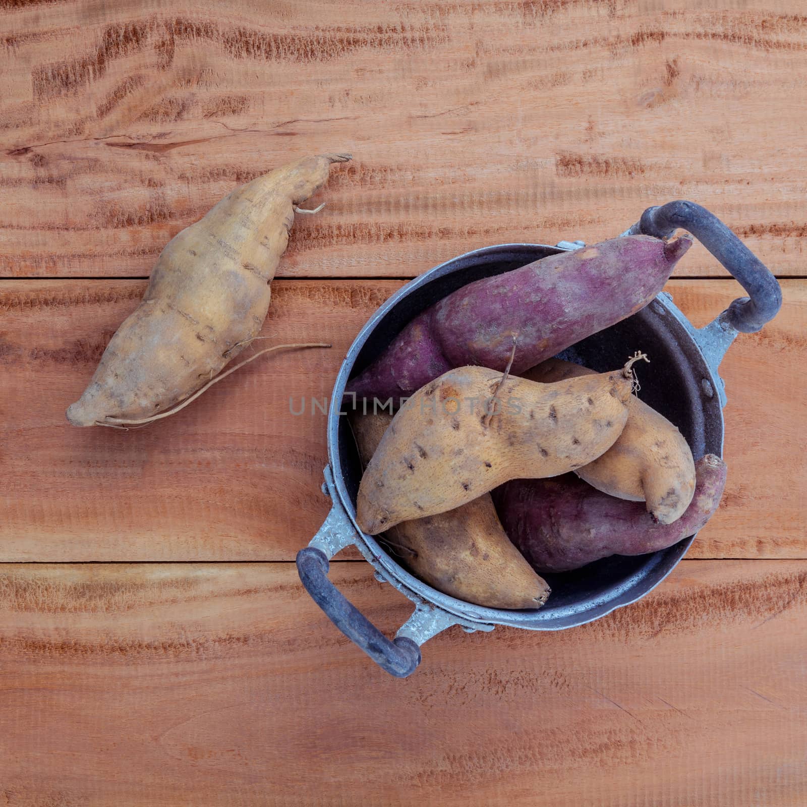 Harvested organic sweet potatoes in the old pot on rustic wood table.