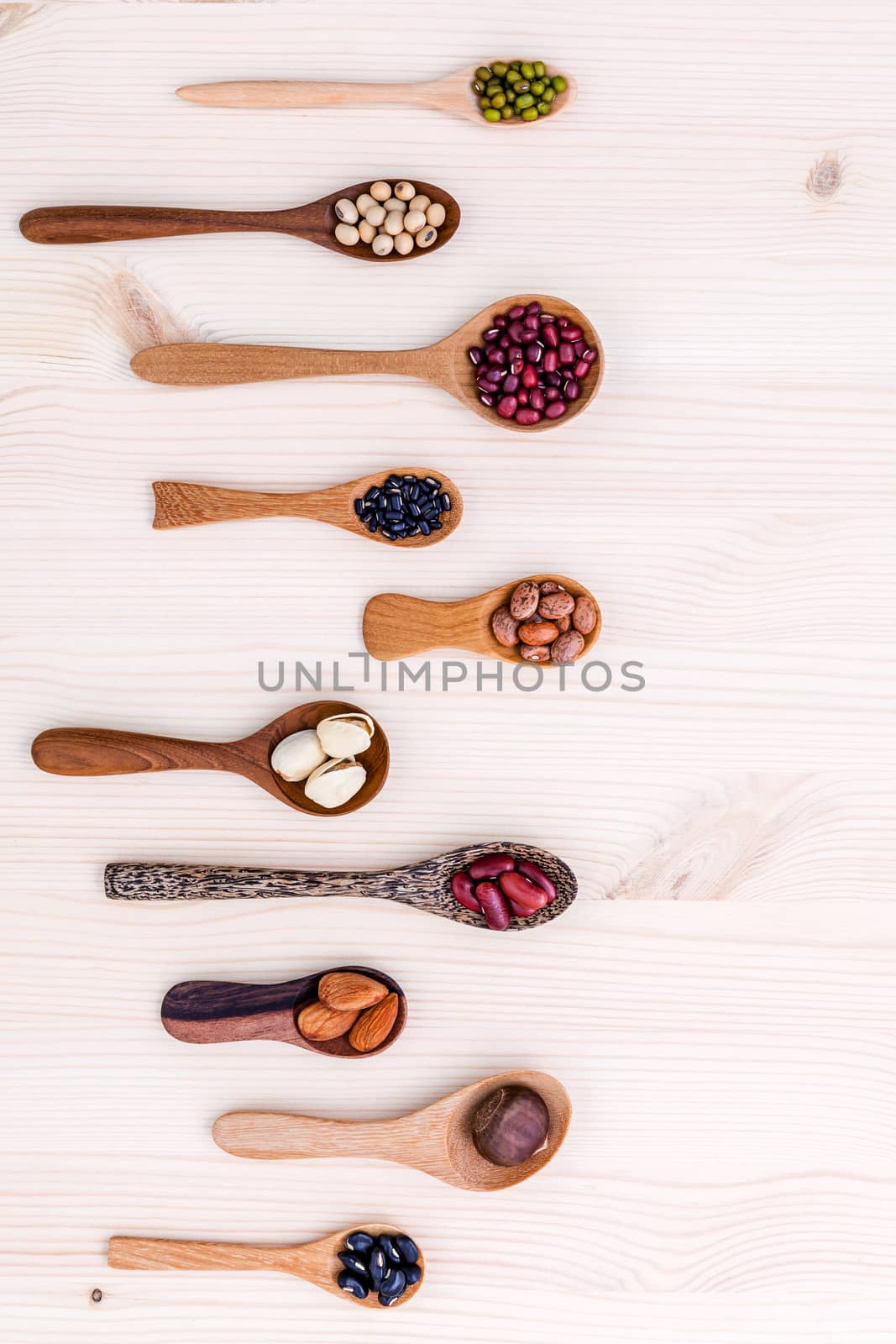Assortment of beans and lentils in wooden spoon set up on wooden background. mung bean,soybean, red kidney bean , black bean ,red bean ,almonds ,pistachio,chestnut and brown pinto beans .