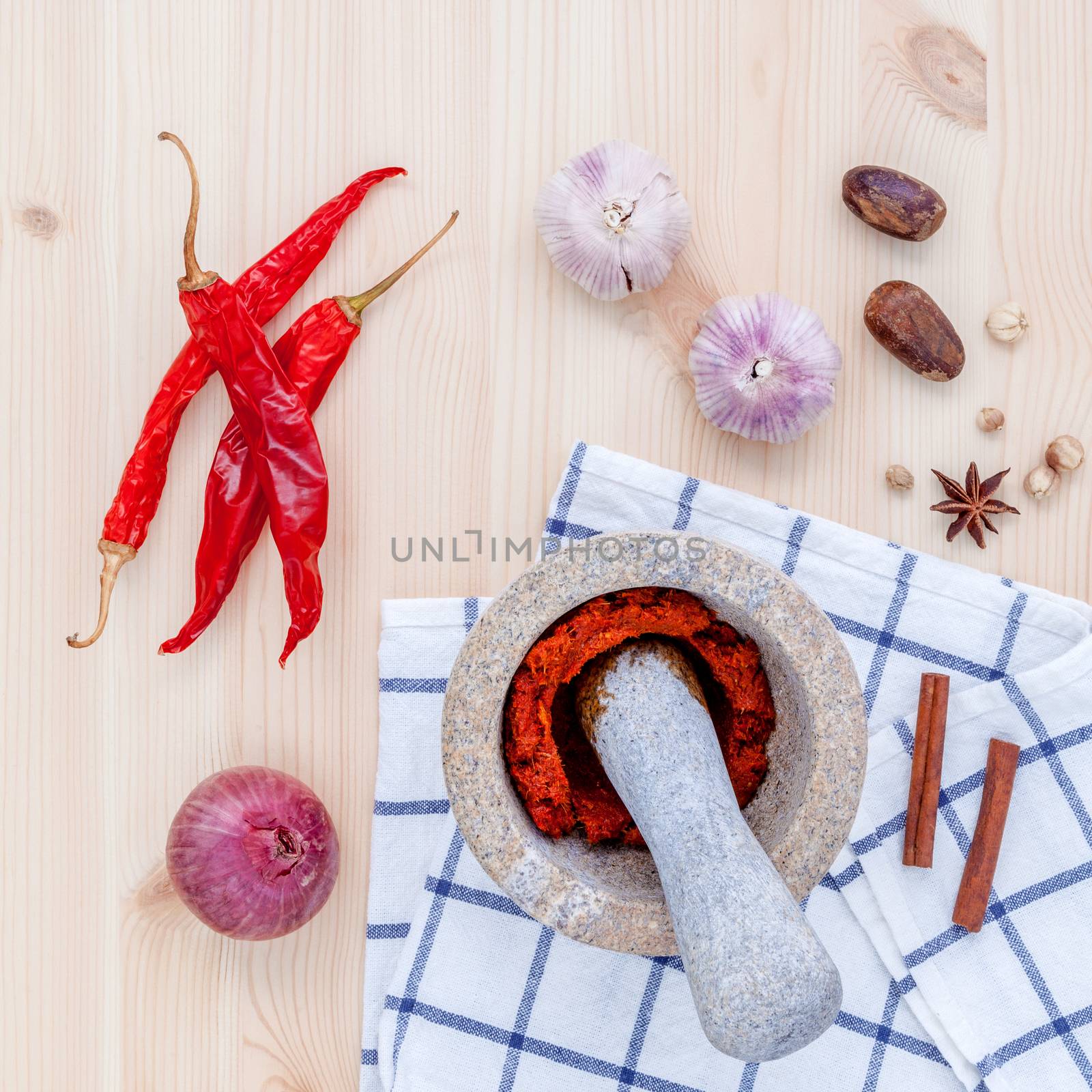 Assortment of spices ingredients and paste of thai popular food red curry with mortar set up on wooden table.