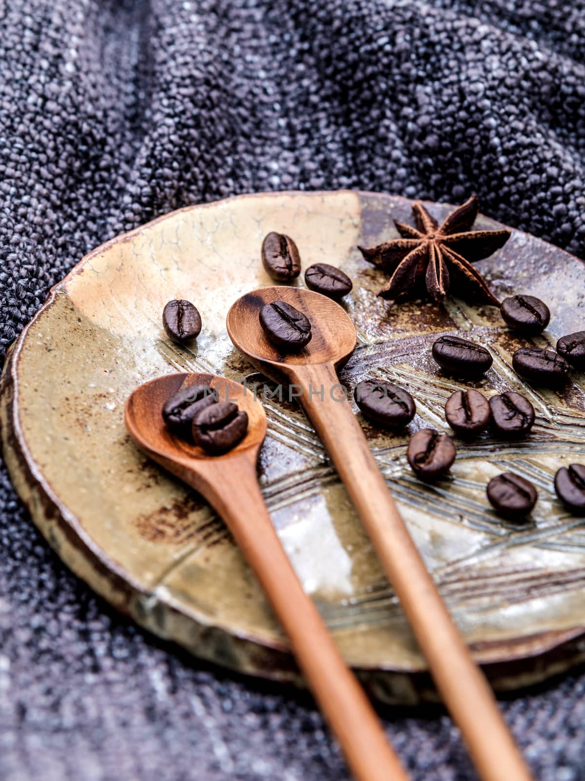 Coffee beans and star anise in ceramic plate with wooden spoons on dark fabric .