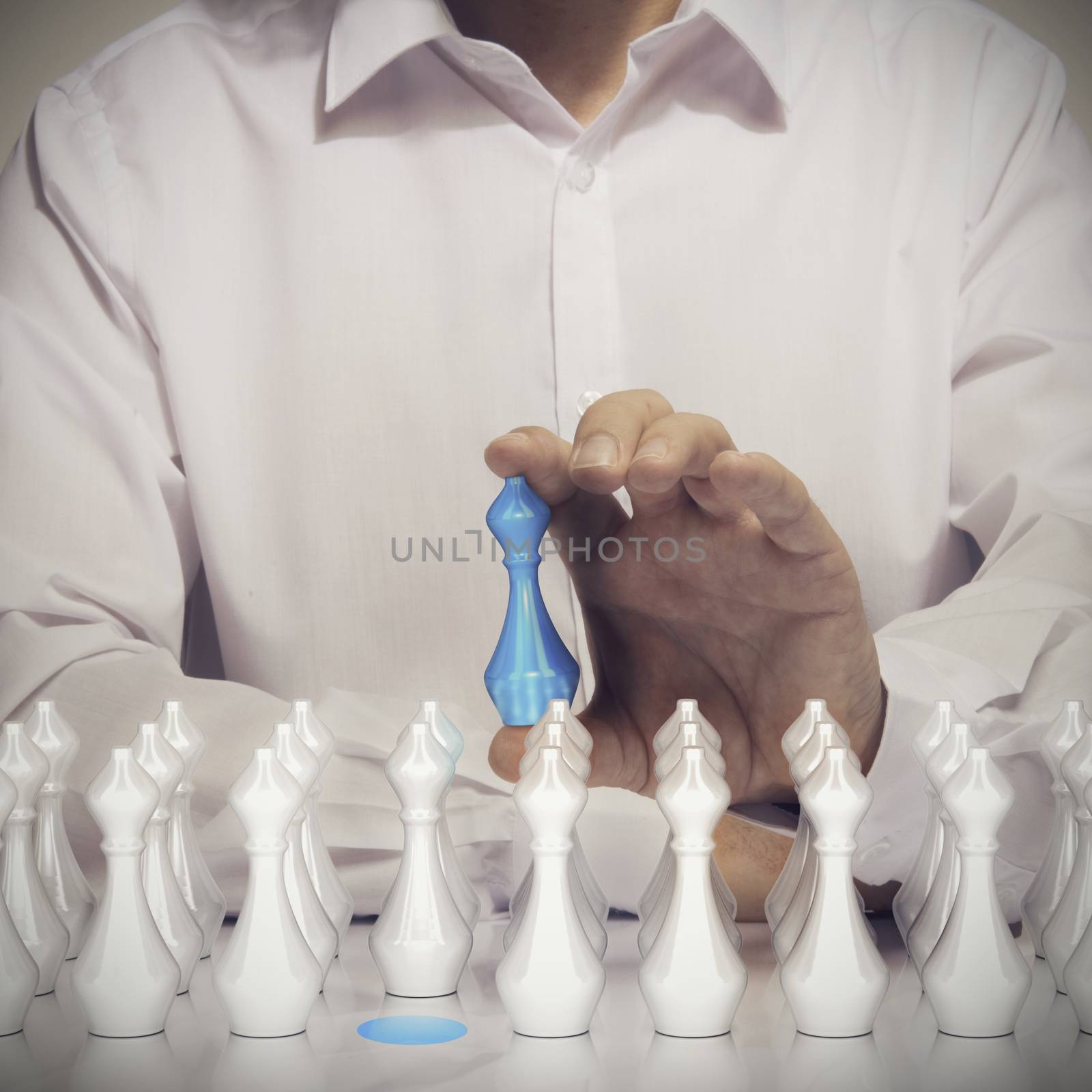Business talents acquisition concept, Conceptual image of a man hand holding a blue pawn with many other white pawns at the foreground. 