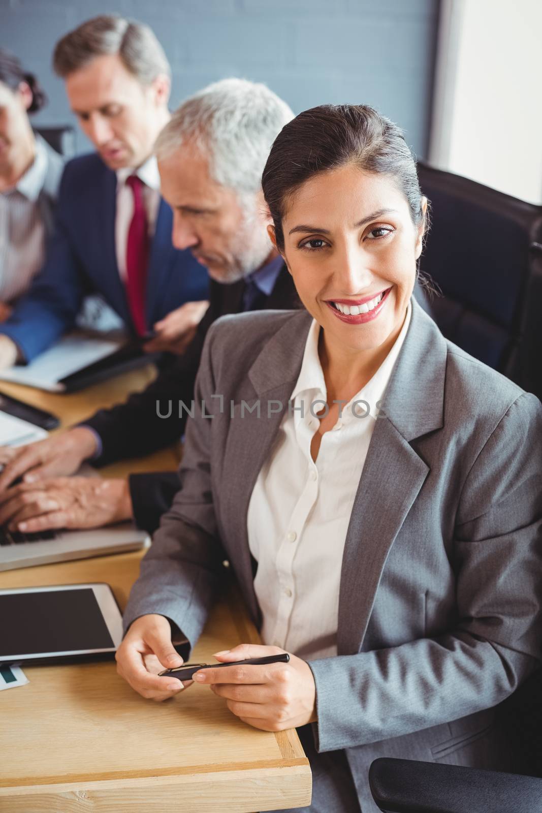 Businesswoman smiling at camera and businesspeople interacting in background in conference room during meeting