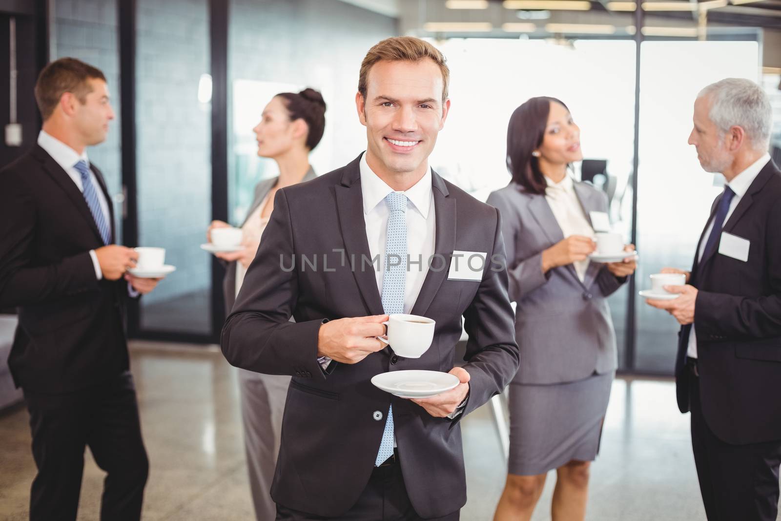 Portrait of businessman having tea during break time and his team interacting in background