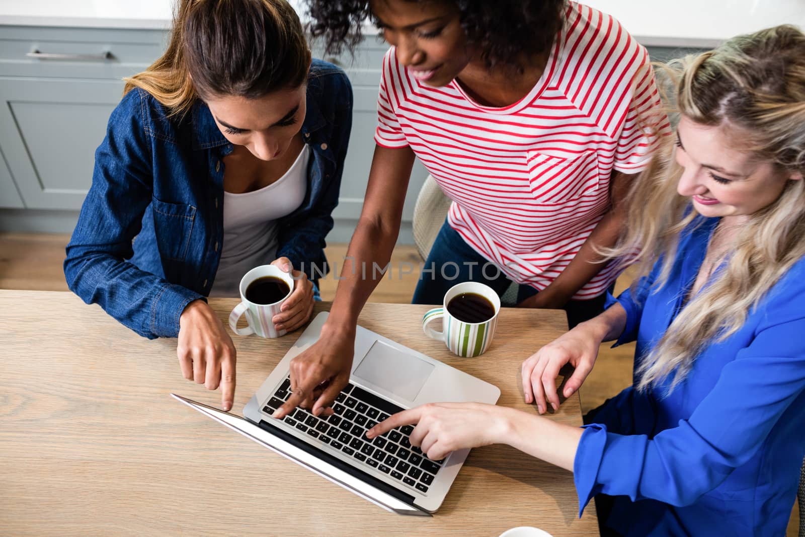High angle view of young female friends using laptop while drinking coffee at home
