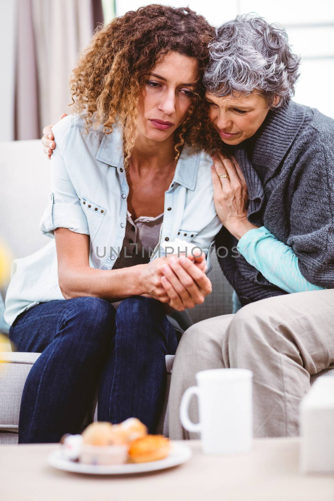 Mother comforting worried daughter sitting on sofa at home