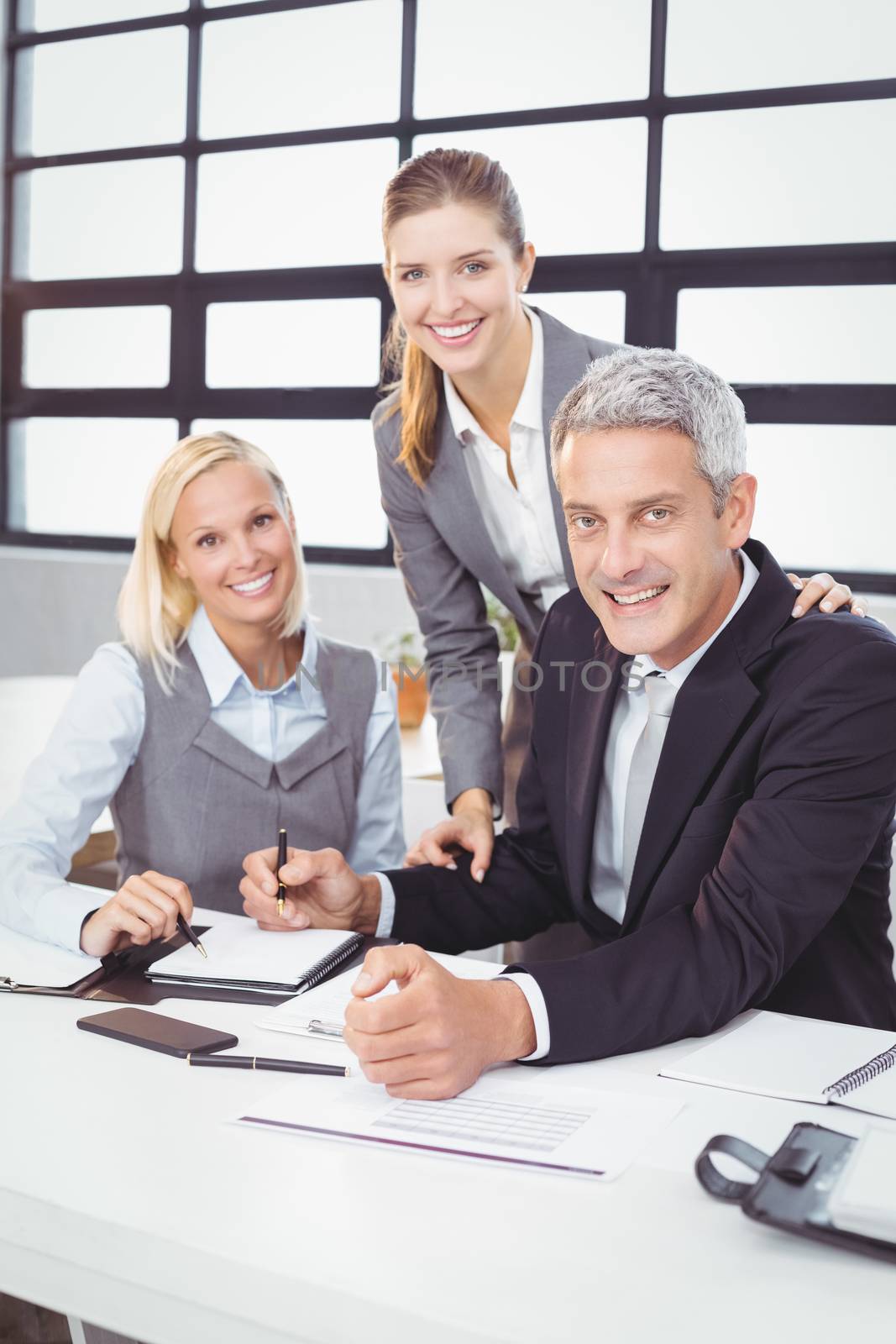 Portrait of happy business people with client at desk in meeting room