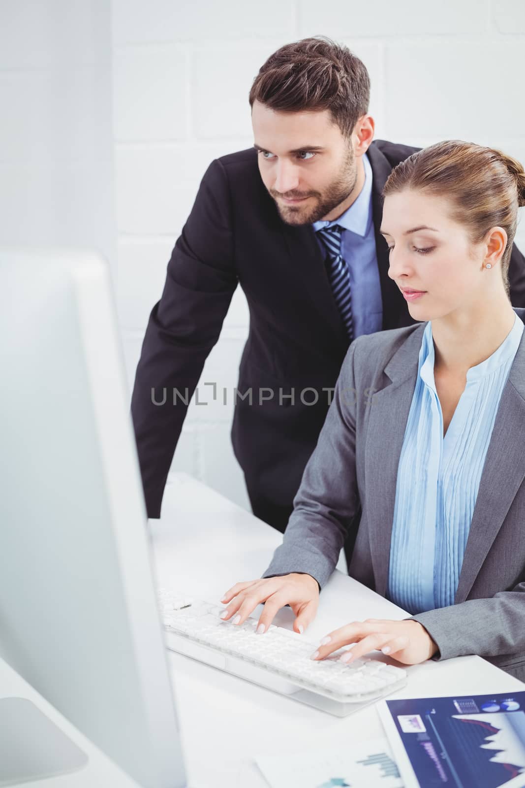 Businessman looking in computer monitor while female colleague typing at desk in office
