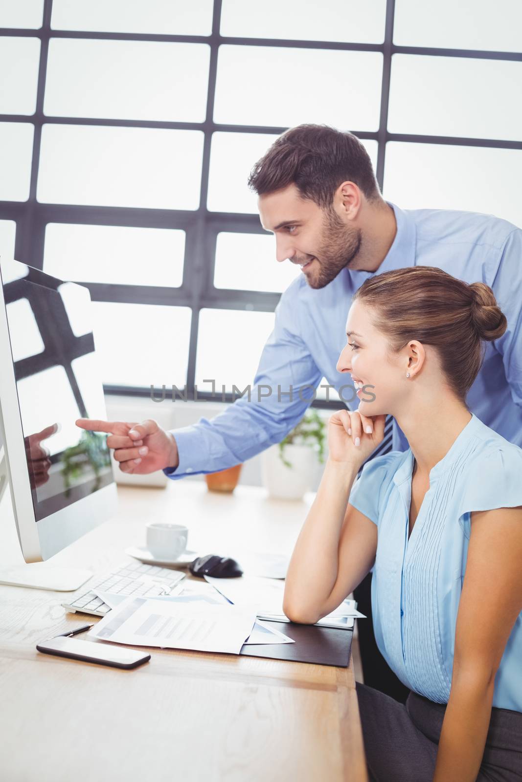 Businessman pointing at computer monitor while explaining female colleague at desk