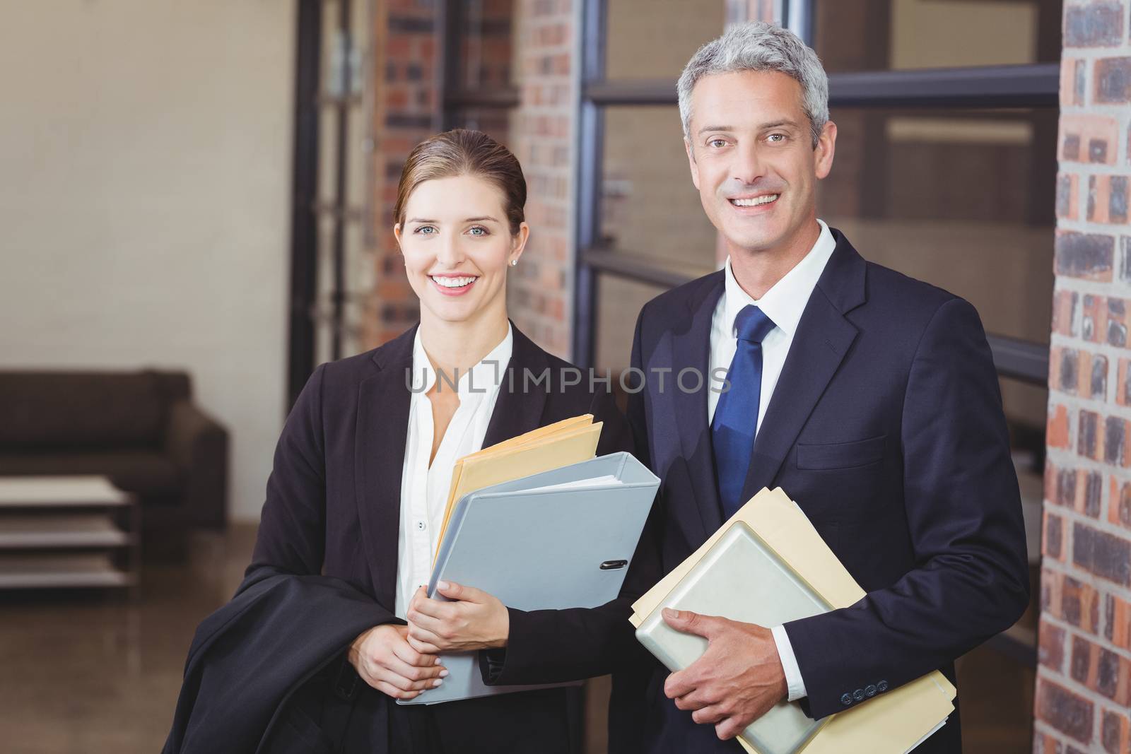 Portrait of happy business people with files standing by window at office