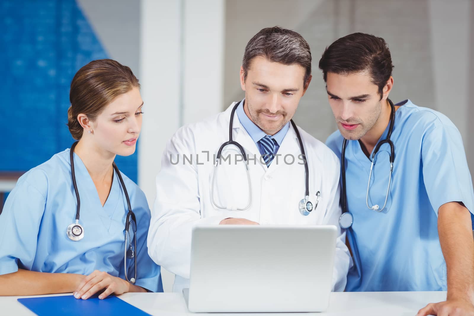 Concentrated doctors using laptop while standing at desk in hospital