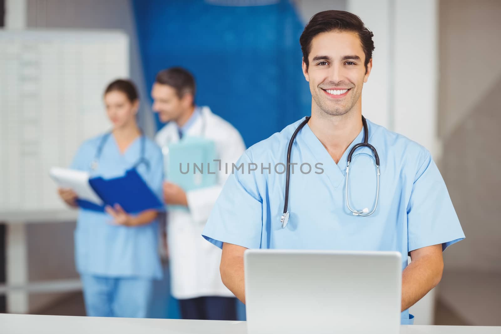 Portrait of happy doctor with laptop and colleagues discussing  by Wavebreakmedia