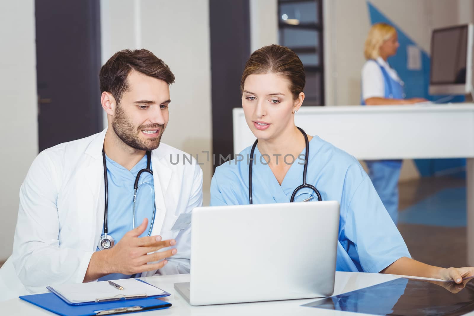 Doctor colleagues using laptop while discussing at desk in hospotal