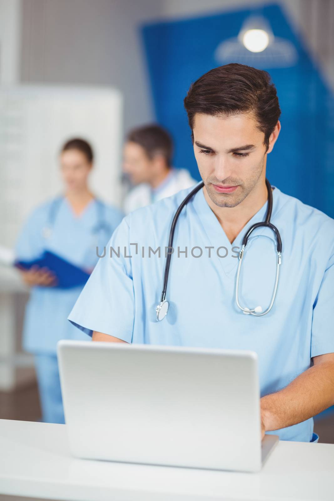 Male doctor working on laptop with colleagues discussing on background