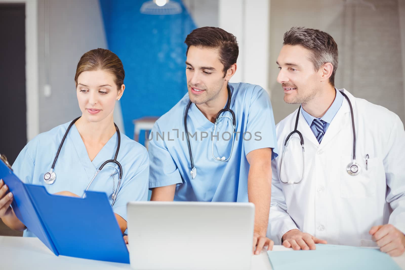 Male doctor and colleagues with clipboard while discussing at hospital