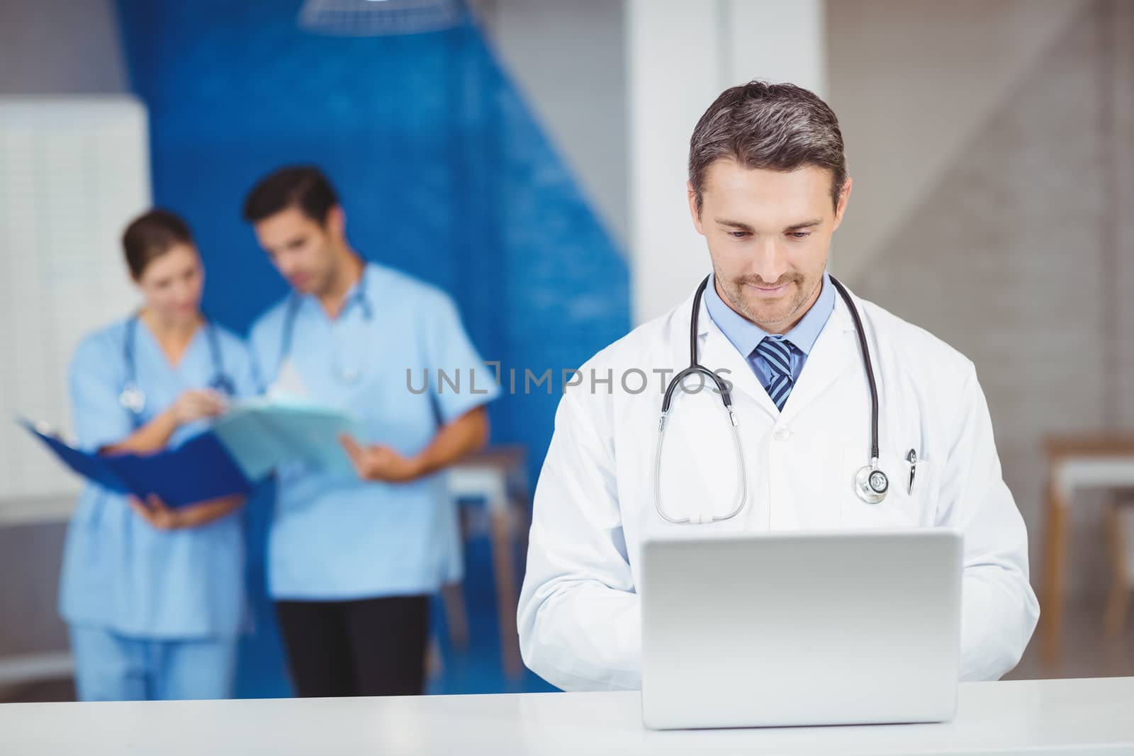 Doctor working on laptop with colleagues discussing by Wavebreakmedia