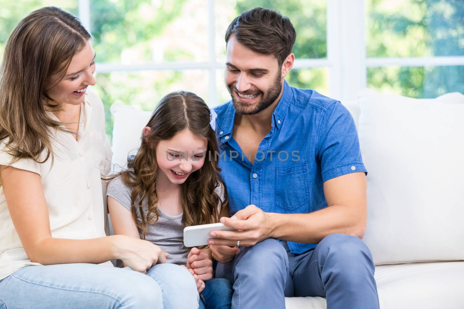 Family looking at smart phone while sitting on sofa by Wavebreakmedia