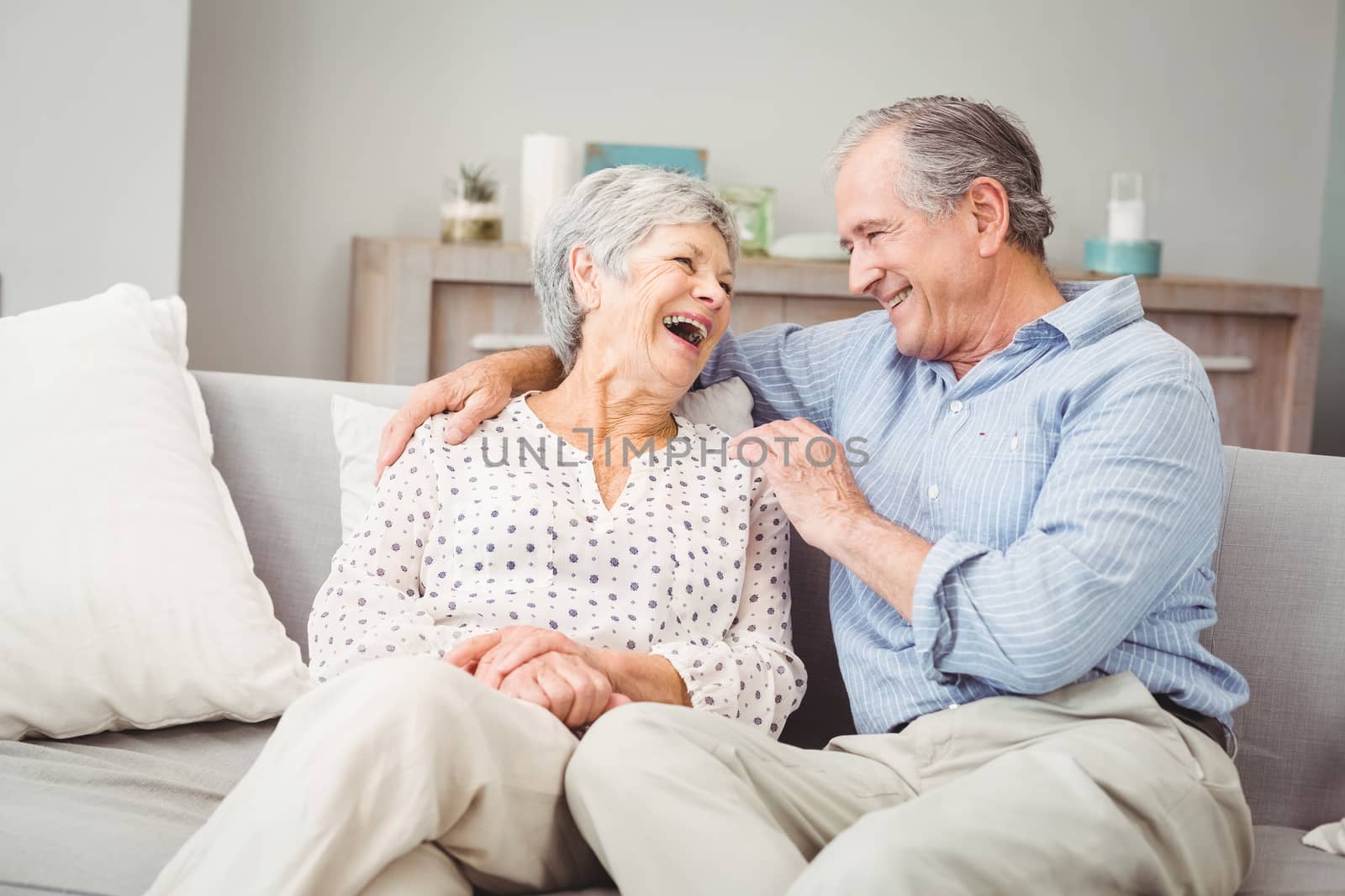 Romantic senior couple laughing while sitting on sofa by Wavebreakmedia