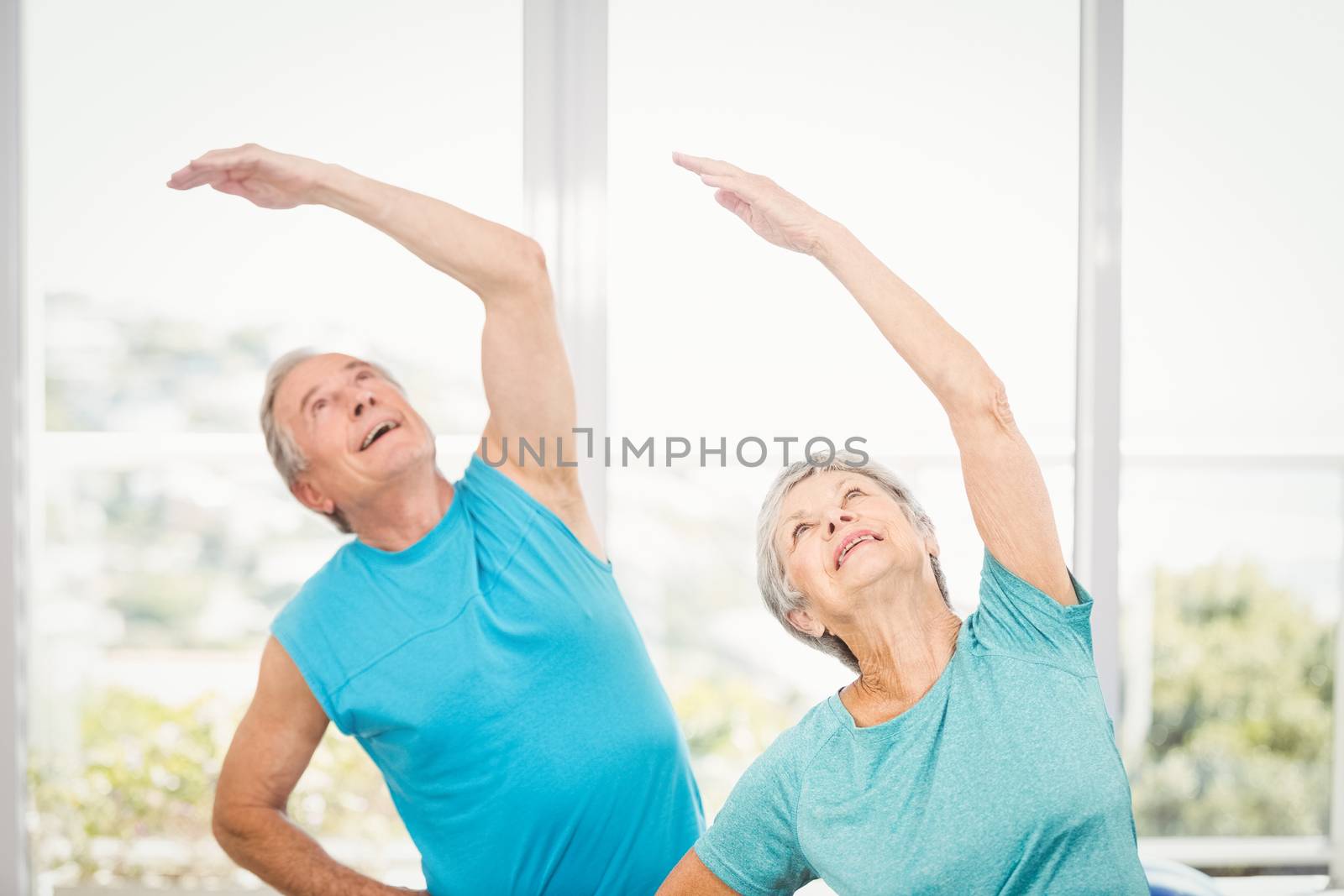 Senior couple with arms raised while exercising at home