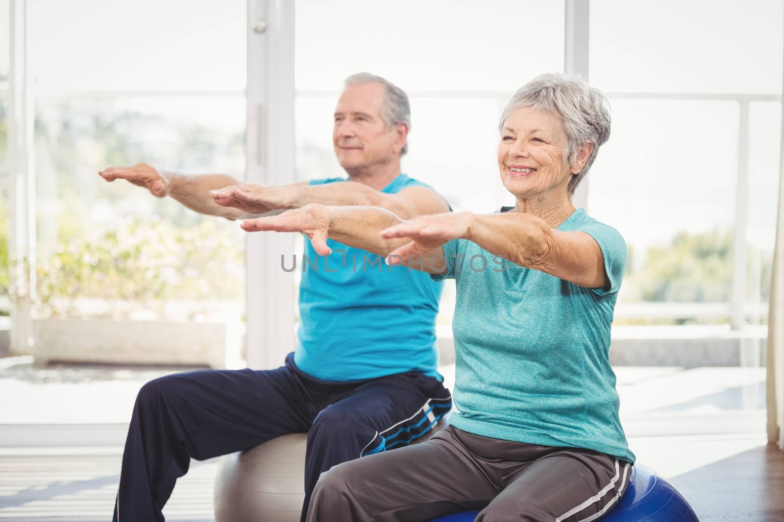 Happy senior couple performing exercise while sitting on exercise ball at home