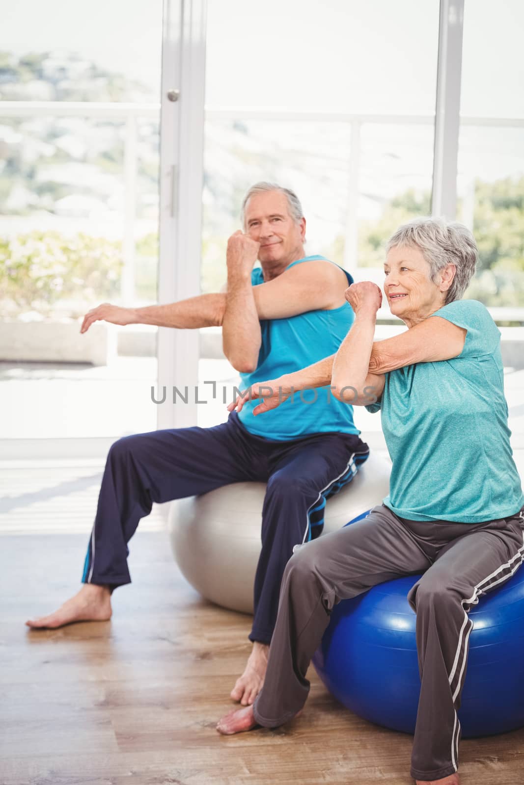 Portrait of senior man exercising with wife while sitting on exercise ball at home
