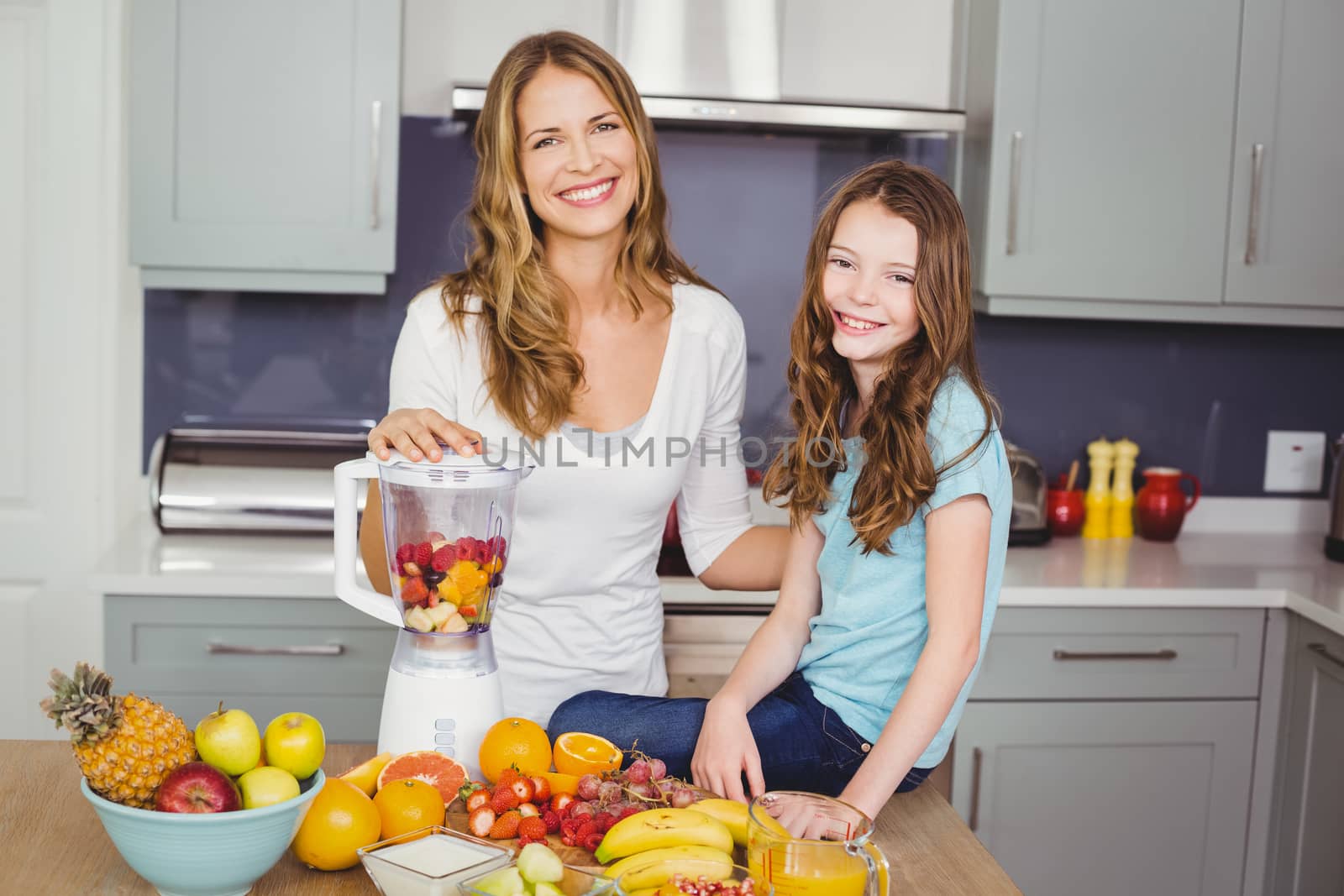 Portrait of happy mother and daughter preparing fruit juice by Wavebreakmedia