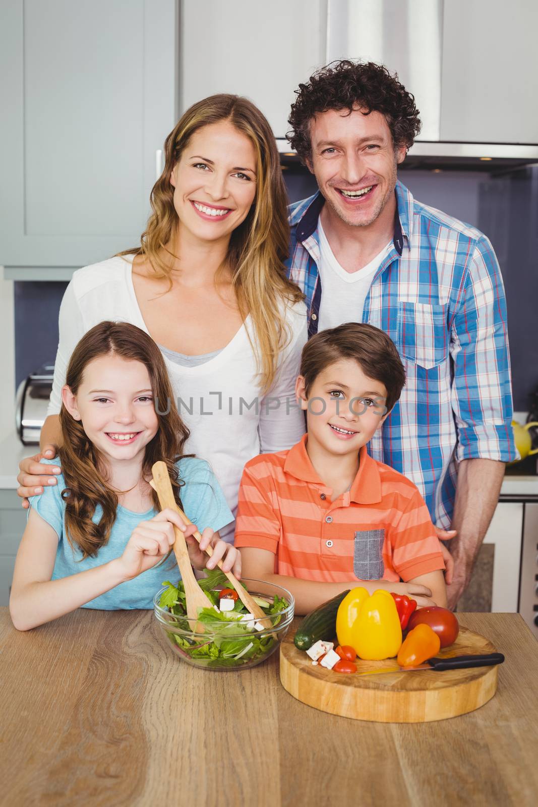 Portrait of happy family preparing vegetable salad in kitchen at home