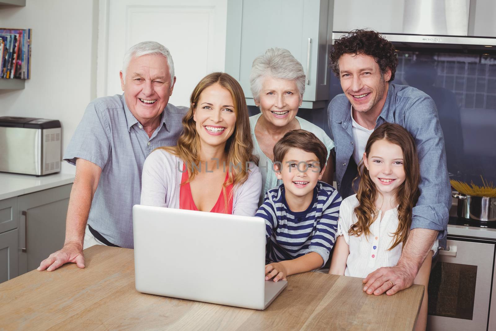 Portrait of happy family using laptop on table in kitchen at home