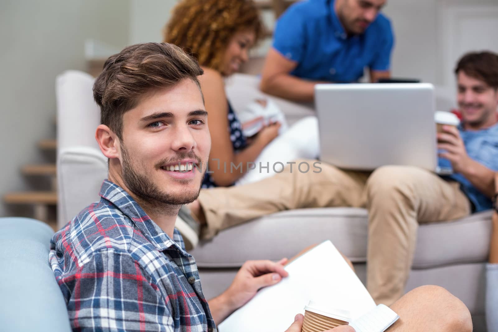 Portrait of happy young man with book while friends in background