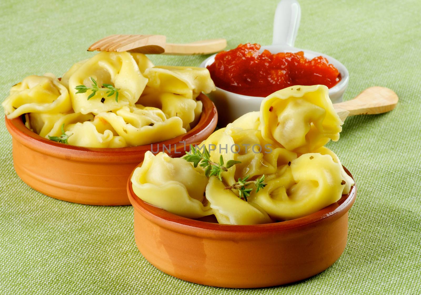 Delicious Meat Cappelletti with Herbs in Ceramic Bowls, Tomatoes Sauce and Wooden Forks closeup on Green Napkin background