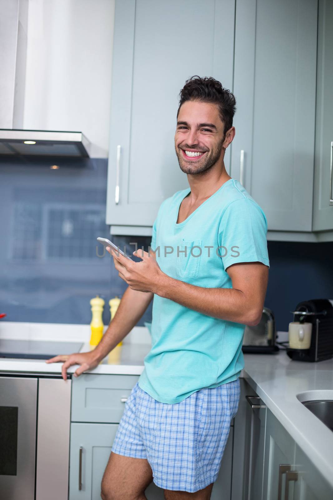 Portrait of smiling young man with phone while standing in kitchen