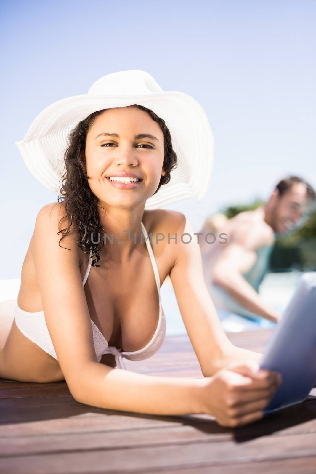 Portrait of happy woman in hat using digital tablet by pool side on a sunny day