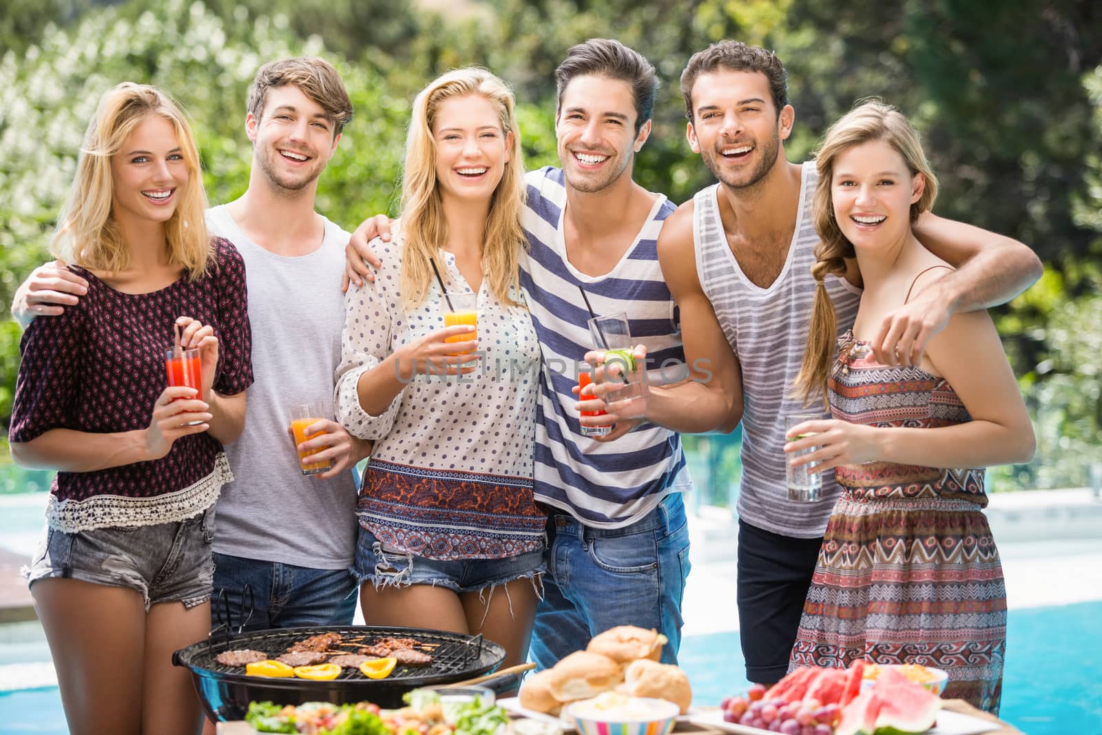 Portrait of friends having juice at outdoors barbecue party near pool