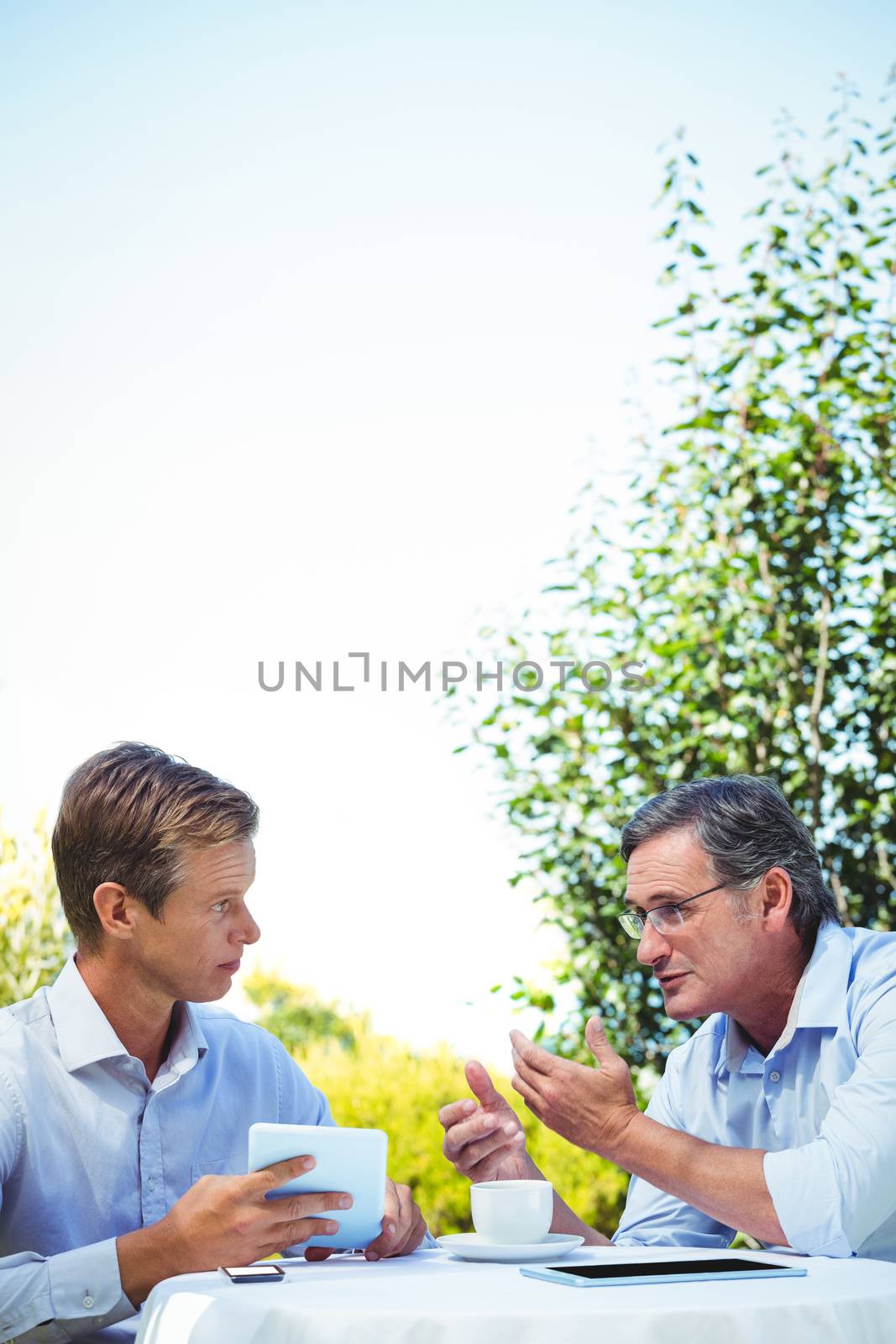 Two businessmen meeting in a restaurant using tablet in the garden