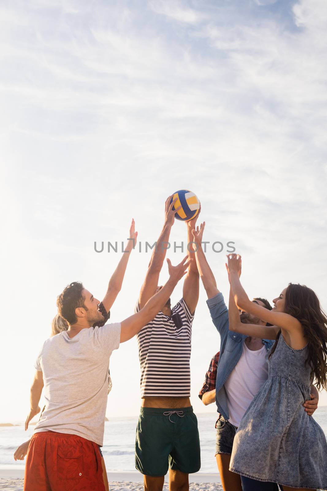 Happy friends playing beach volleyball by Wavebreakmedia