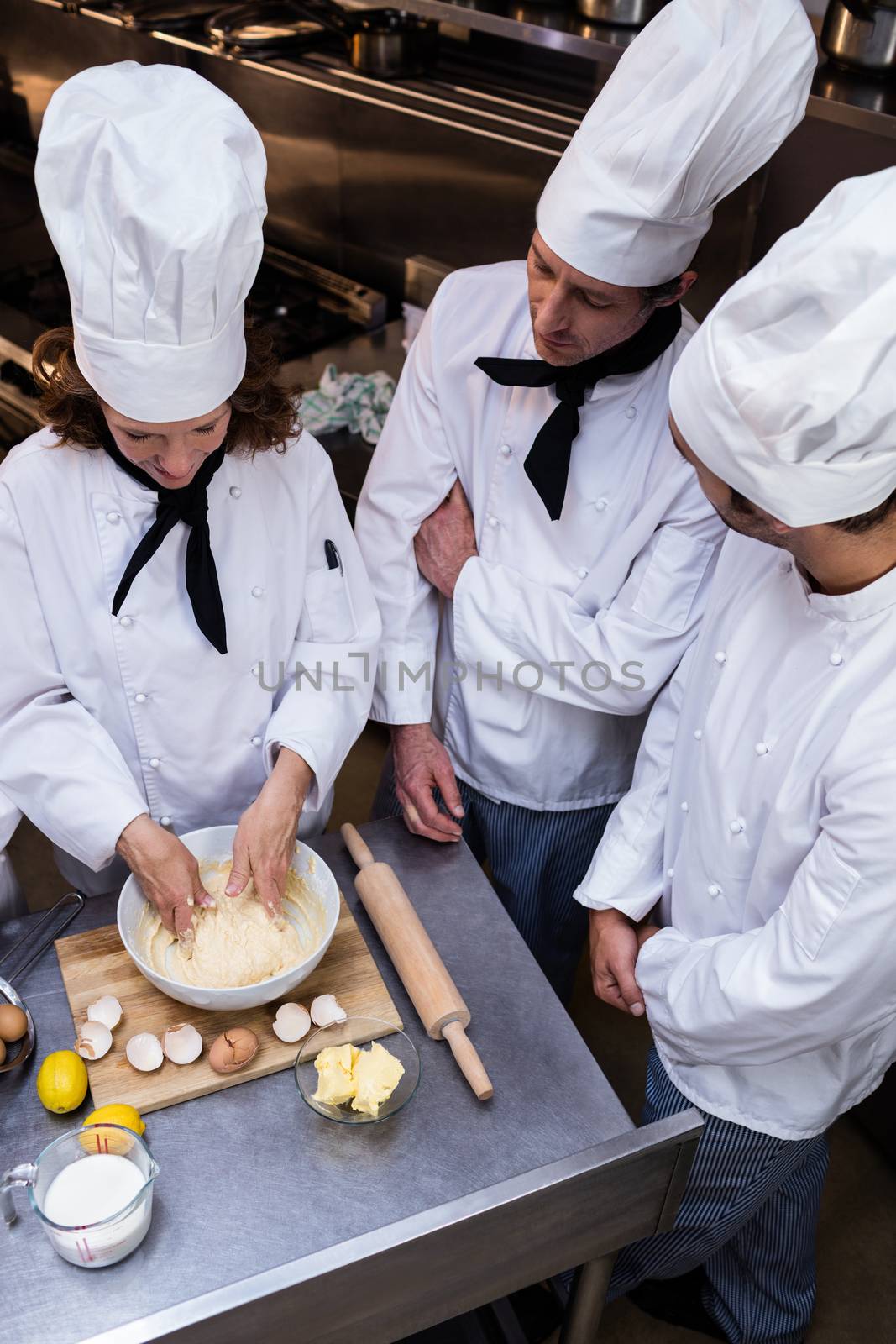 Head chef in commercial kitchen teaching his team to prepare a dough