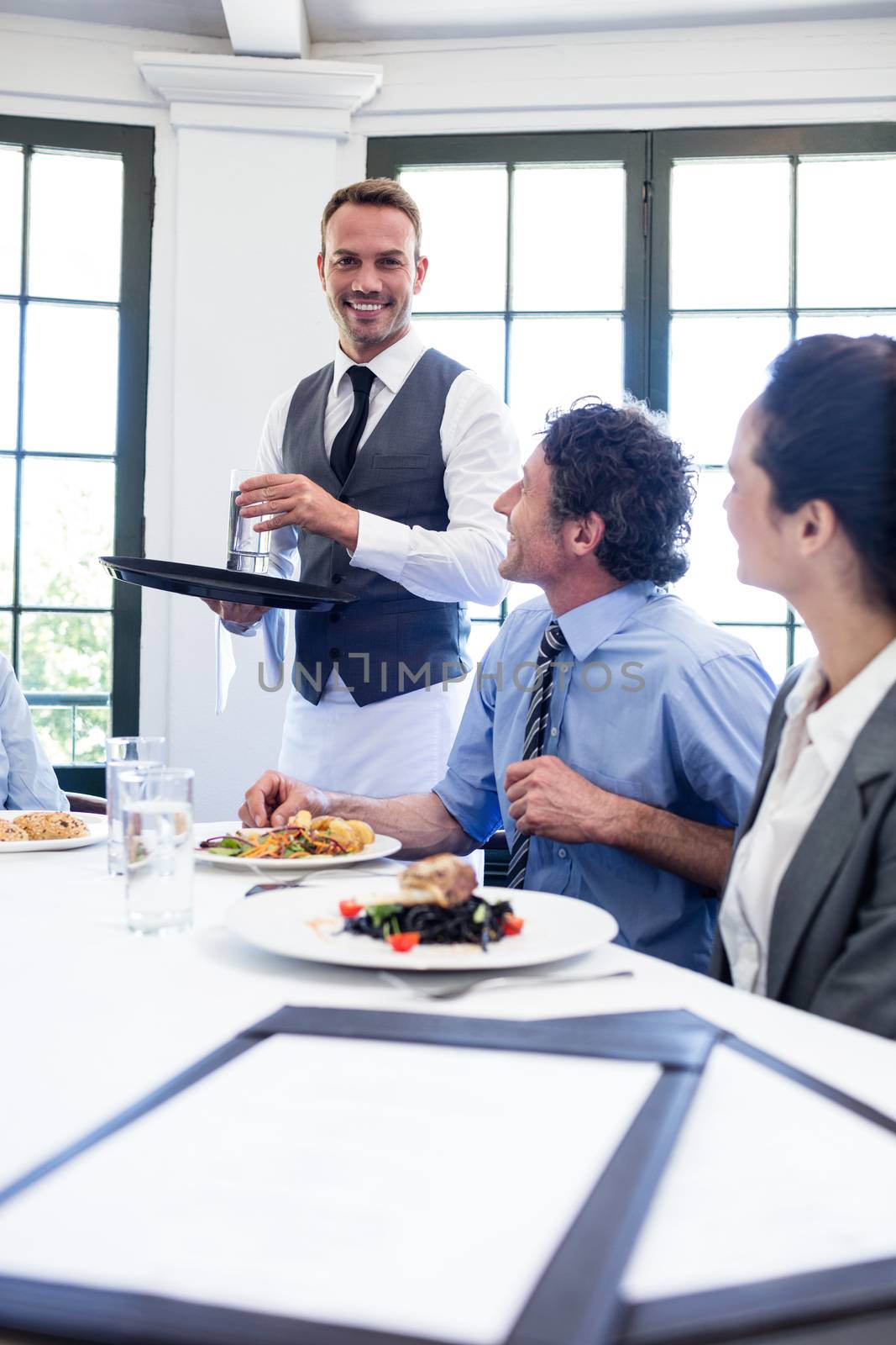 Waiter serving water to business people by Wavebreakmedia