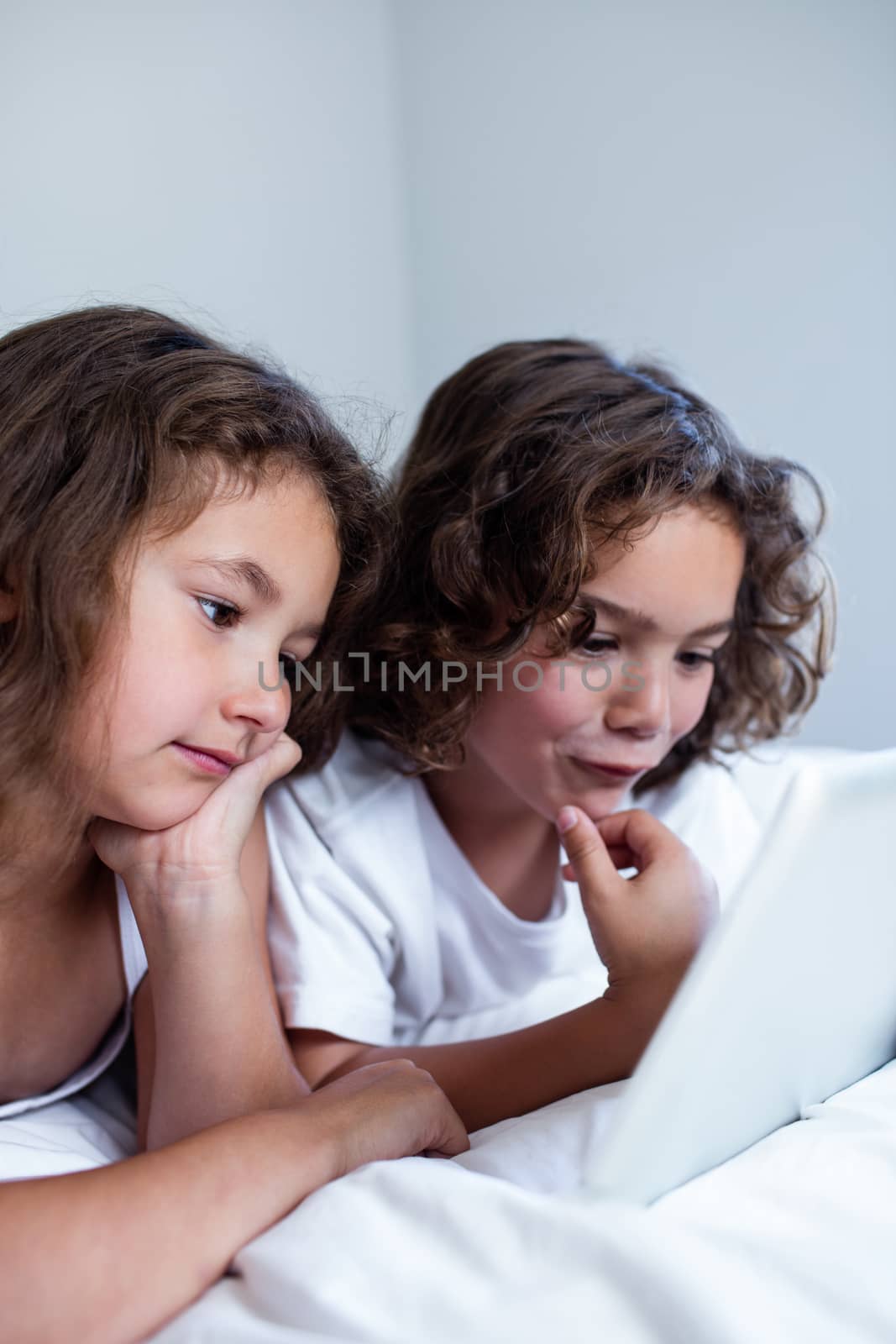 Brother and sister using digital tablet on bed in bedroom