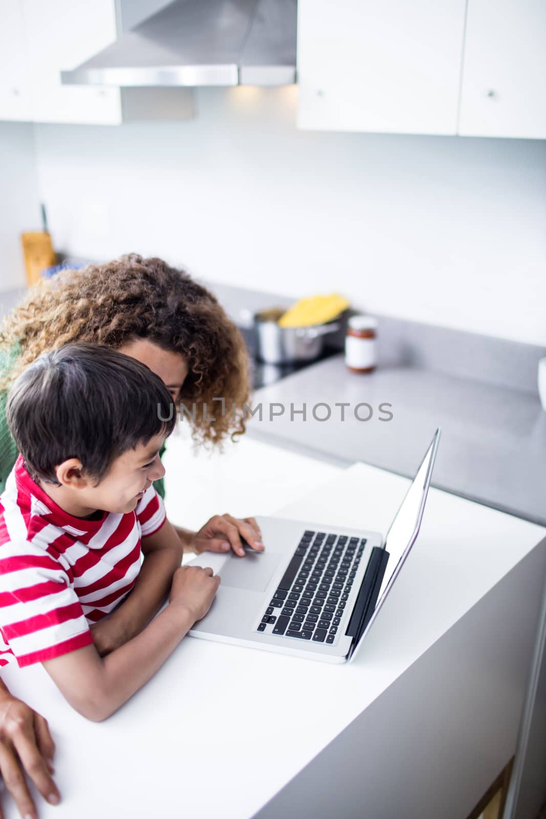 Mother and son using laptop in kitchen at home
