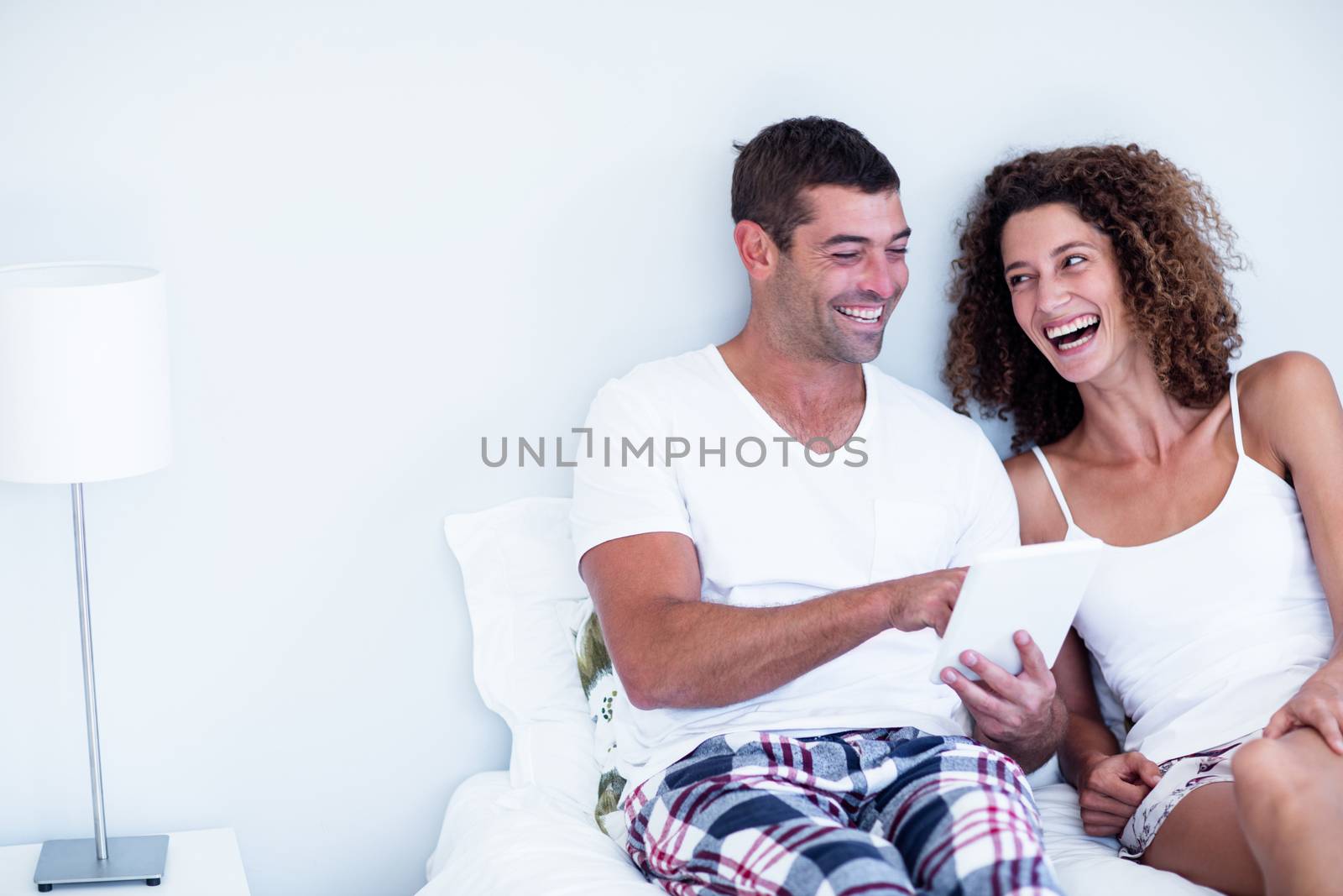 Happy couple using digital tablet on bed in bedroom