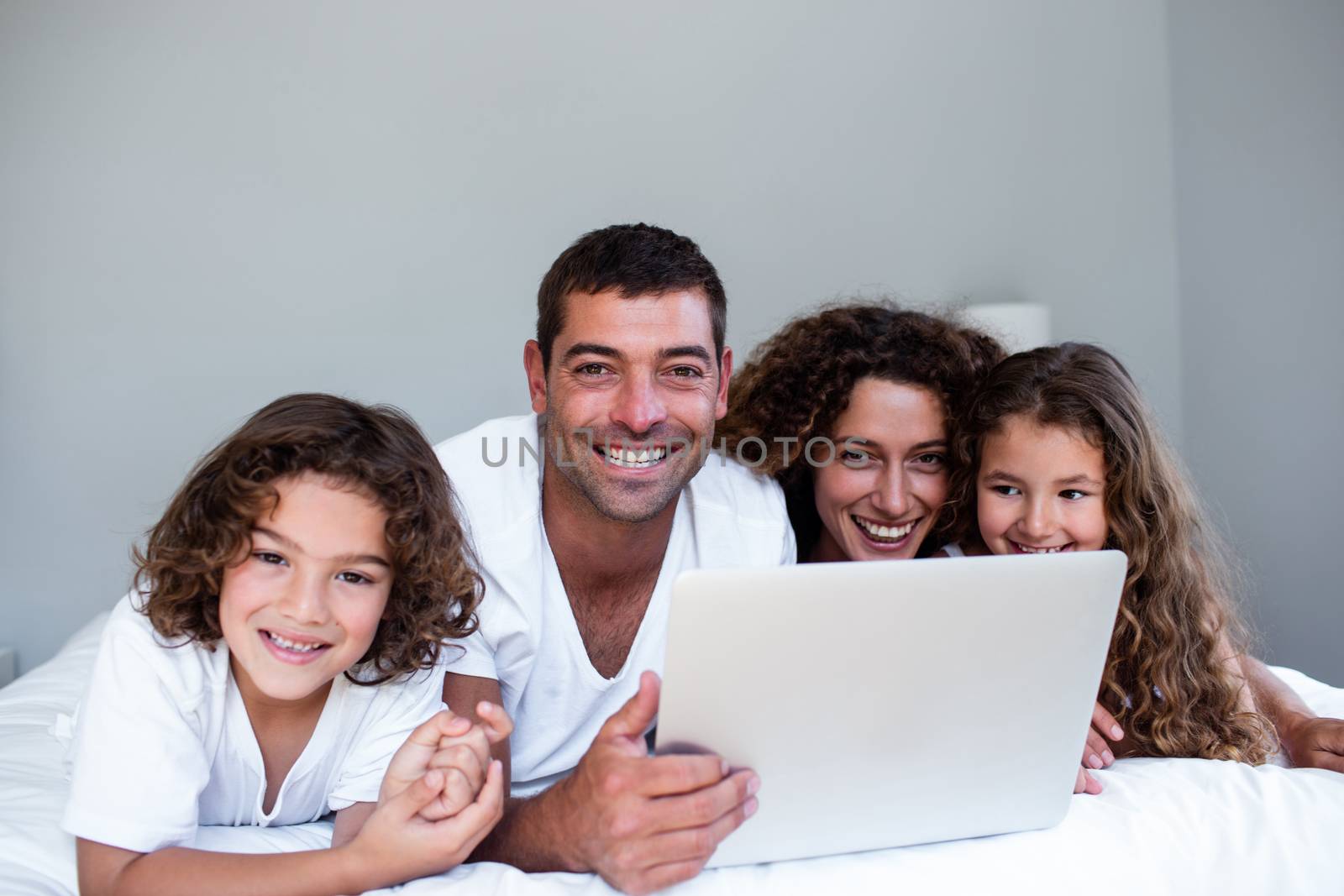 Portrait of family using laptop together on bed in bedroom
