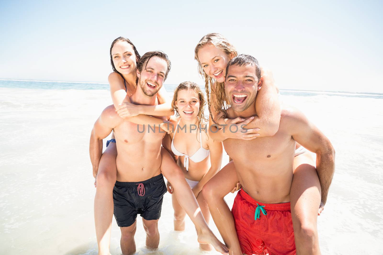 Men giving a piggy back to women on the beach by Wavebreakmedia